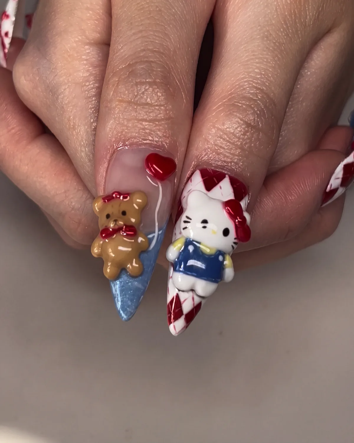 Hello Kitty in blue overalls and a tan bear sculpted on XL stiletto nails, one argyle, one blue cat-eye